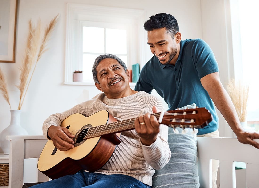 We Are Independent - Cheerful Son Watching his Senior Father Playing the Guitar as They Spend Time Together at Home